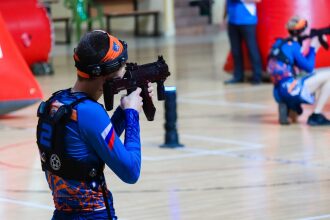 Боец LASERWAR целится из-за синего игрового препятствия.